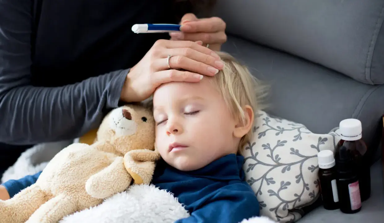 Bambino dorme con orsacchiotto, la mamma controlla la febbre. L'antibiotico fa sudare, ma la guarigione è vicina.