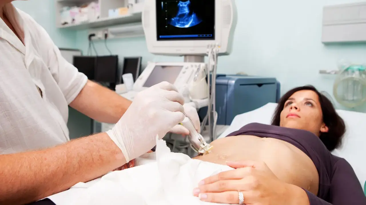 Medico esegue ecografia guidata per una biopsia fegato. La paziente è sdraiata, mentre il medico usa una sonda ecografica.