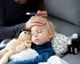 Bambino dorme con orsacchiotto, la mamma controlla la febbre. L'antibiotico fa sudare, ma la guarigione è vicina.