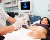 Medico esegue ecografia guidata per una biopsia fegato. La paziente è sdraiata, mentre il medico usa una sonda ecografica.