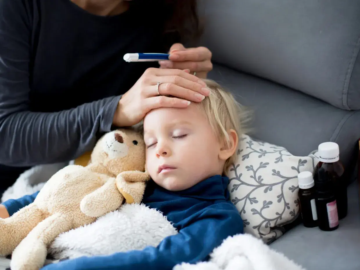 Bambino dorme con orsacchiotto, la mamma controlla la febbre. L'antibiotico fa sudare, ma la guarigione è vicina.