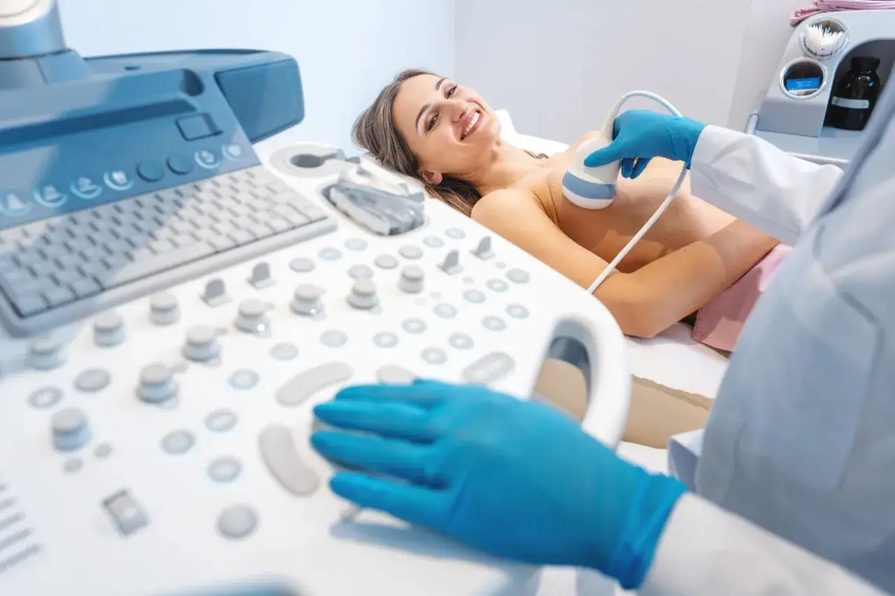 Ecografia al seno: un medico con guanti blu usa una sonda per un ago aspirato. La paziente sorride.