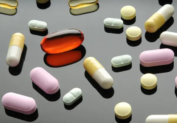 Varie pillole e capsule colorate, tra cui una grande capsula arancione trasparente. Un'immagine che fa riflettere sulla terapia biologica cos'è.