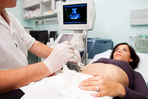 Medico esegue ecografia guidata per una biopsia fegato. La paziente è sdraiata, mentre il medico usa una sonda ecografica.